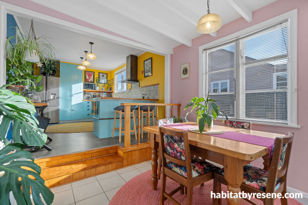 Dining area and kitchen with soft pink and bright yellow walls, and blue cabinetry.
