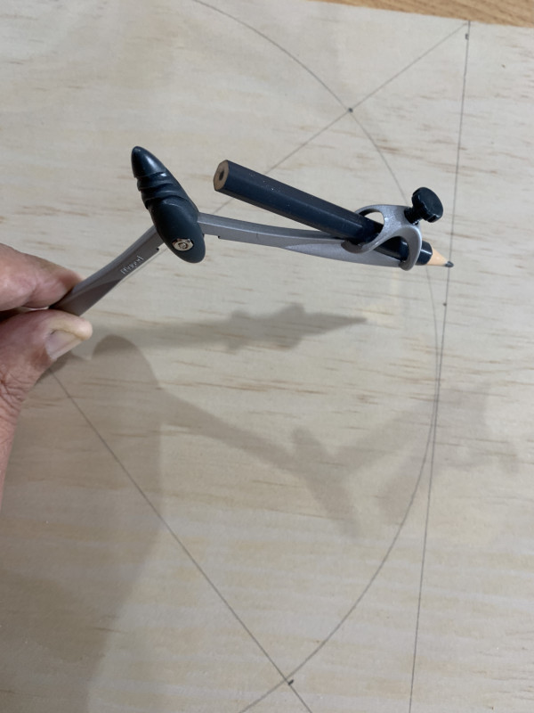 A person drawing a curve with a compass on a piece of wood