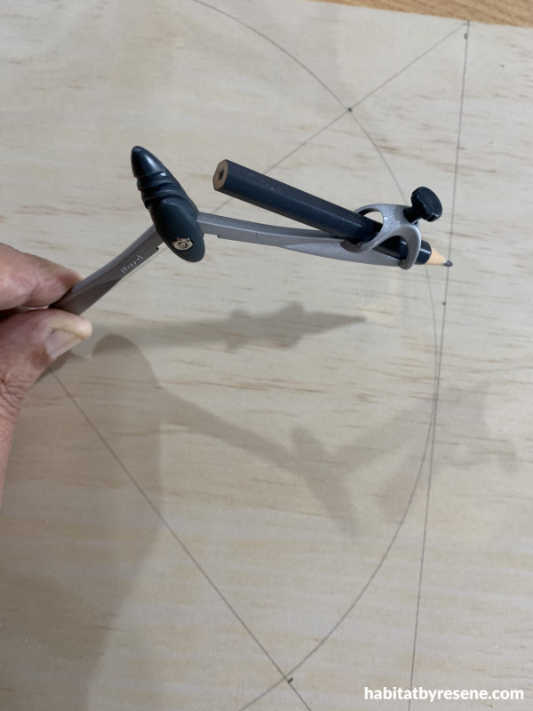 A person drawing a curve with a compass on a piece of wood