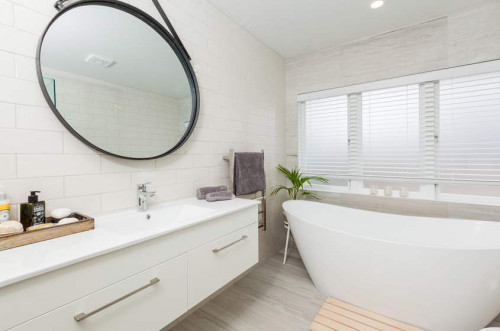 white bathroom, freestanding bath, hanging mirror, white tiles, curved bath